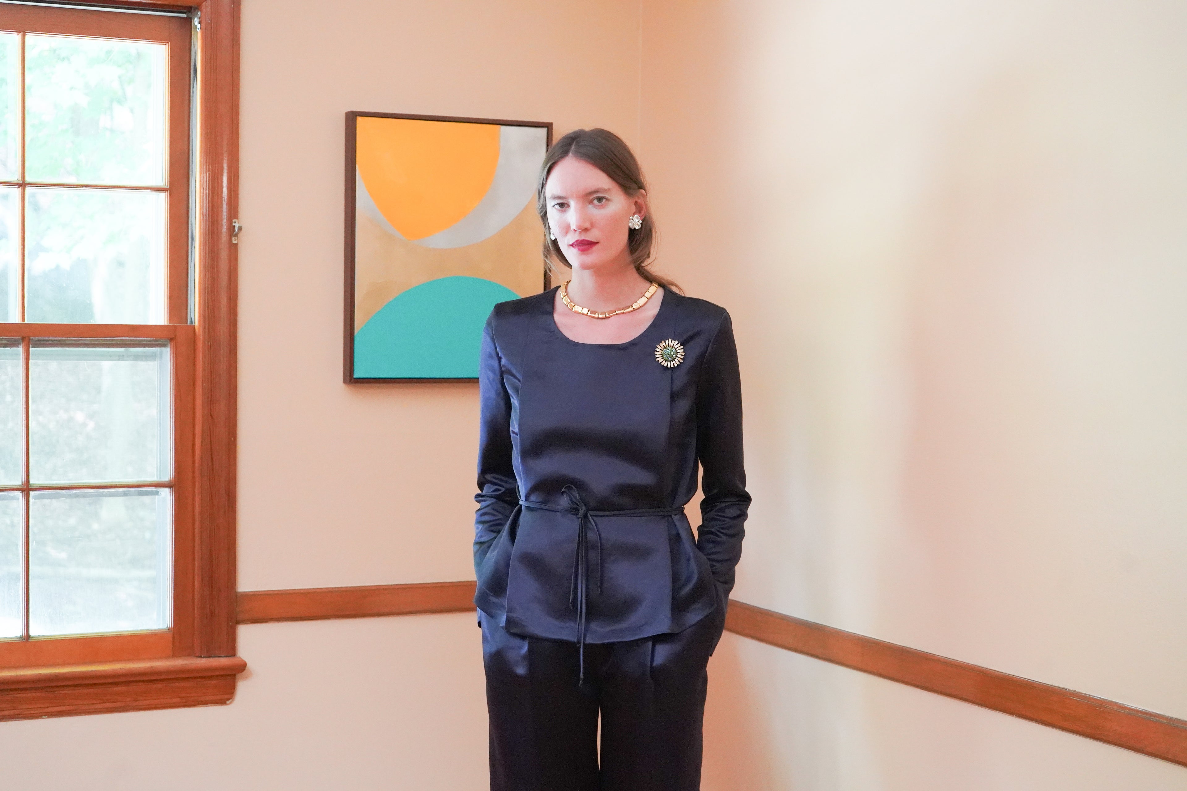 Dark navy satin long-sleeve top with a tie waist and matching dark trousers, relaxed with hands in pants side pockets.