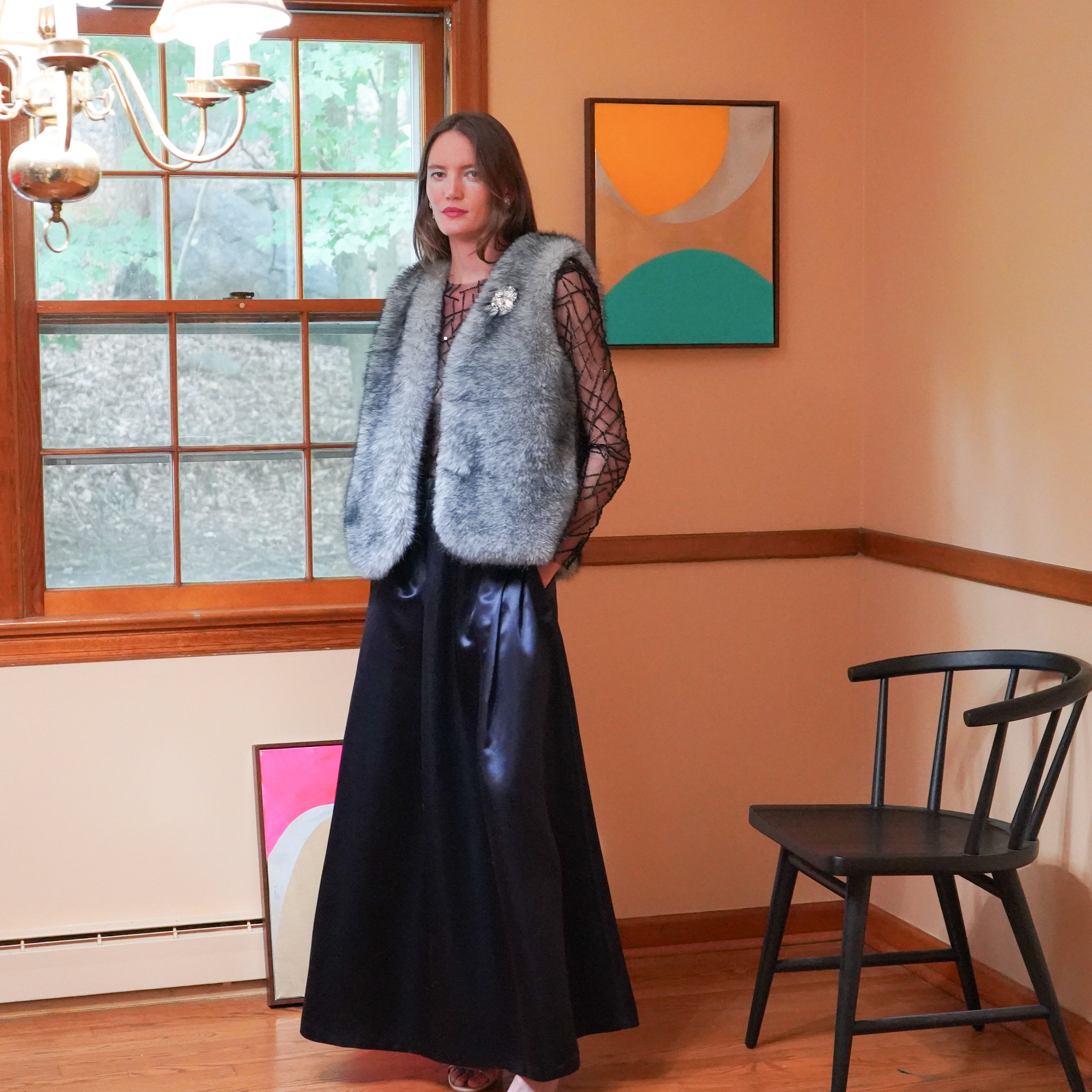 gray fuzzy faux-fur vest over a sheer black long-sleeve top and a long dark navy charmeuse skirt. 